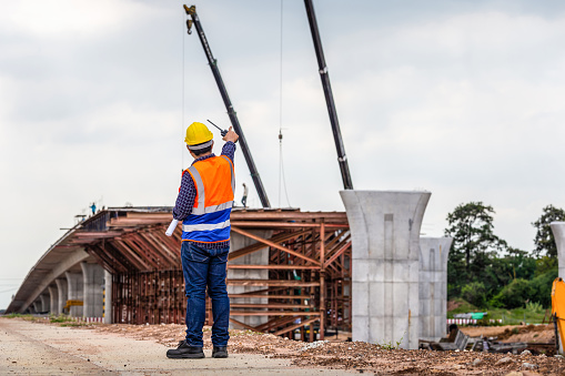 Rear view of Engineer under inspection and checking project at the building site, Foreman worker in hardhat at the infrastructure construction site