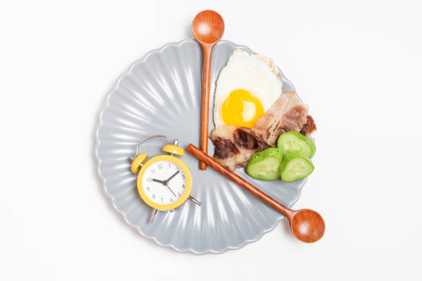istock Clock shaped wooden spoons on plate with food on a white background top view, intermittent fasting concept. 1472233110