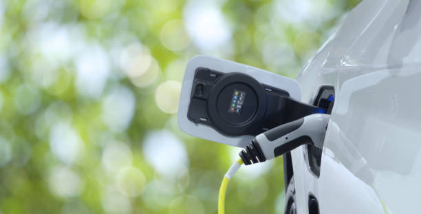istock Close-up EV plug connected white modern EV Car for recharging battery energy on blurred greenery background 1472233438