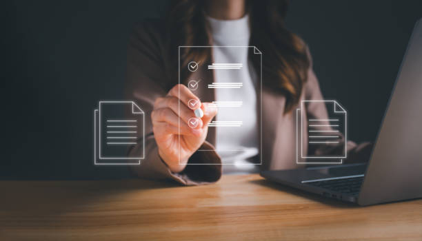 istock Businesswoman working on laptop with electronics document icons by virtual notebook screen using a stylus pen checking list on a digital tablet. E-document management Paperless workplace concept. 1472239260