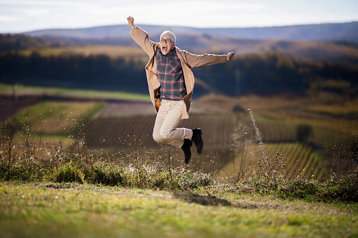 Cheerful mature woman having fun while screaming and jumping during autumn day on a hill. Copy space.