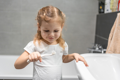 Happy toddler girl brushing teeth in the bath. High quality photo