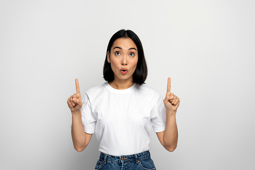 Wow, look above at advertisement. Portrait of pleasantly surprised girl pointing up and looking with shocked face, showing copy space for commercial. Indoor studio shoot isolated