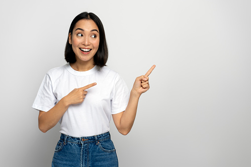 Cheerful positive woman pointing fingers away showing space for your advertisement, having toothy smile. Indoor studio shot isolated on white background