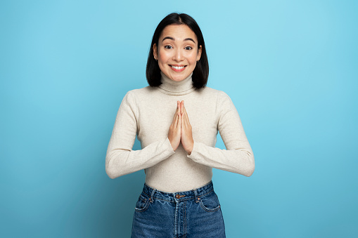 Portrait of attractive woman praying, begging with pleading grimace, gesture of asking apologising. Indoor studio shot isolated on blue background