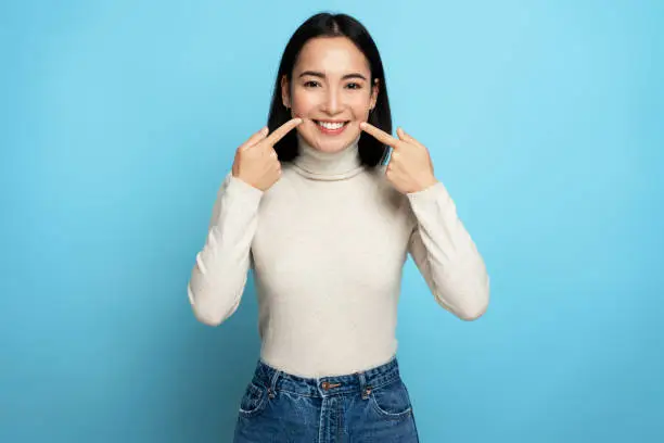 Photo of Portrait of pretty cheerful woman points index fingers at smile shows white teeth