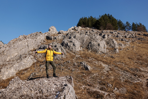 Young man standing with arms raised and enjoying fresh air while hiking on rocky mountain