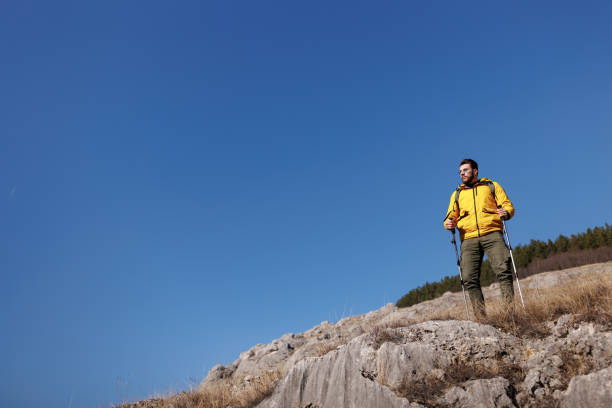 Young man standing and enjoying fresh air on the top of rocky mountain