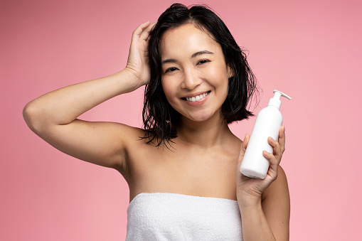 Asian woman holding hair conditioner before applying. Woman hold bottle shampoo and conditioner. Beauty product, balm bottle. Young woman advertising care product