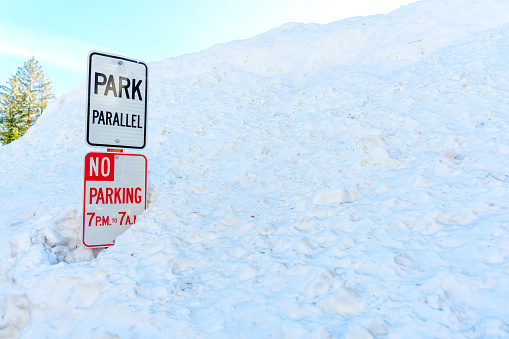 No Parking and Park Parallel signs in a deep snowdrift. Reminder to skiers and snowboarders of the park's boundaries and safety guidelines.