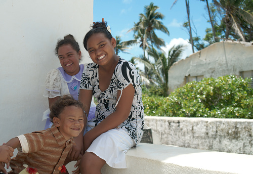 Aitutaki Cook Islands - november 9 2010;; Island children sitting happily outside church smiling and waving.