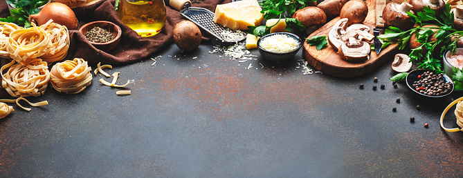 Food background. Uncooked pasta, brown mushrooms, vegetables, cheese and ingredients for tasty cooking on brown table background, top view. Copy space banner