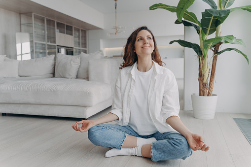 Peace of mind and mental health concept. Young european woman is practicing yoga on floor and smiling. Meditation, consciousness and relaxation at home. Posture exercise, lotus asana.