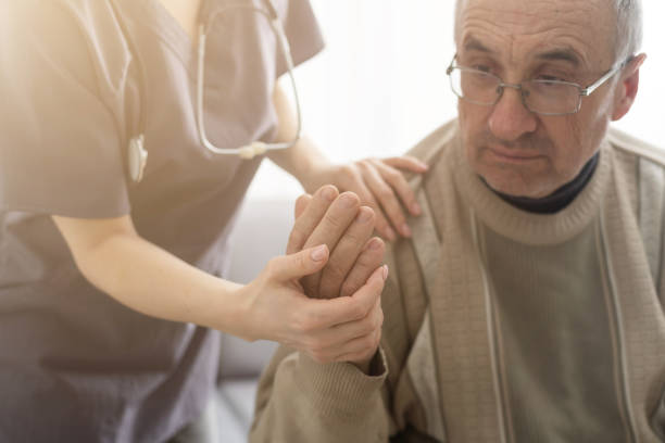 Caring nurse talks to old patient holds his hand sit in living room at homecare visit provide psychological support listen complains showing empathy encouraging. Geriatrics medicine caregiving concept stock photo