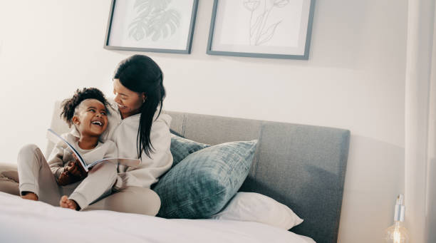 istock Woman smiles at her child while helping her read a book 1472261568