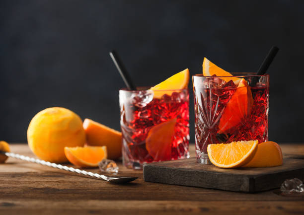 cóctel negroni en vasos de cristal con rodaja de naranja y naranjas crudas frescas sobre tabla de cortar con colador sobre fondo de madera. - summer party drink umbrella concepts fotografías e imágenes de stock