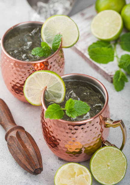 istock Moscow mule cocktail in a copper mug with lime and mint and wooden squeezer on light background with steel shaker 1472262409