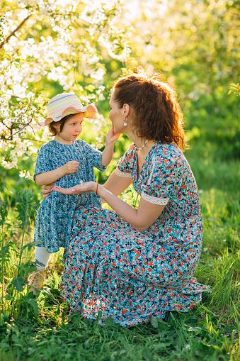 a mother and little daughter in a hat on a walk in the spring garden. the concept of maternal love care. happy childhood. clothes for children and mothers.