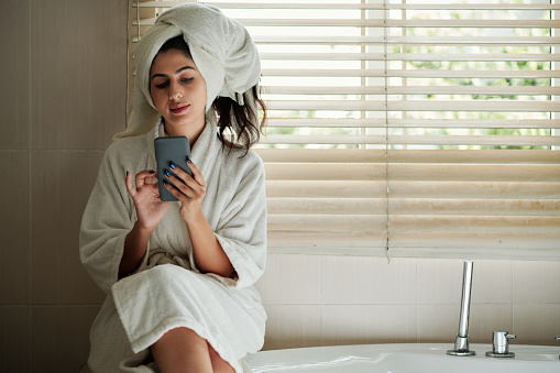 Young woman in bathrobe checking social media after taking bath in the evening