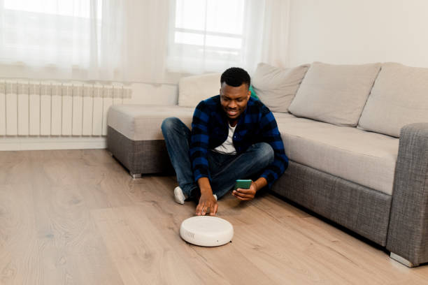 istock Happy young African American setting up his smart vacuum cleaner 1472264320