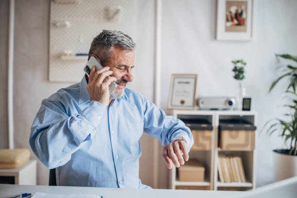 istock Senior male manager using mobile phone, talking and looking at wristwatch 1472266020