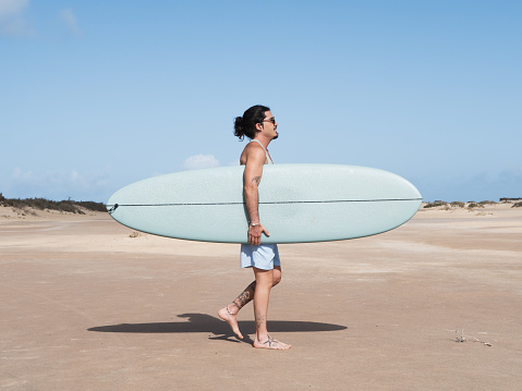 Hispanic surfer walking on the sand holding his surfboard