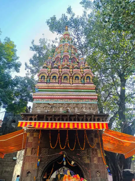 Photo of Inside view of popular holy temple In Maharashtra state tuljabhavani mata Mandir tuljapur. dravidian style temple tower, sculpture of god and goddess on the spire, green trees, sky on background.