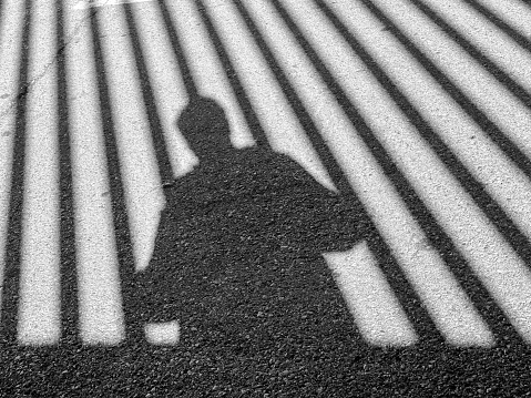 Shadow of man and vertical bars of fence in the street