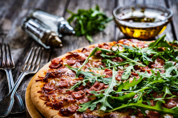 Tasty pizza with ham, white mushrooms, mozzarella and arugula on wooden table stock photo