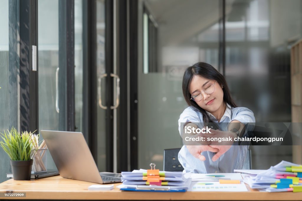 Asian businesswoman feel tired from hard work, thus doing arm stretching posture to relax body. Tired Asia woman stretching her hands while working in office. Adult Stock Photo