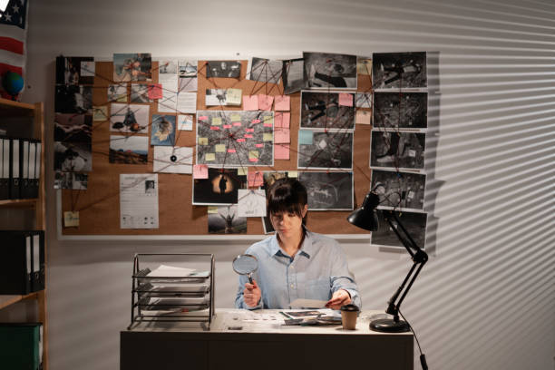 istock Detective in criminology looking for clues with a magnifying glass while working in her office 1472274513