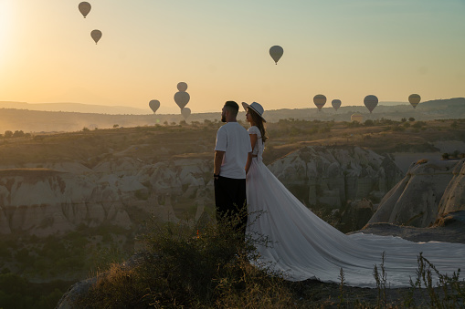 Cappadocia,Turkey-September 20 2022: Beautiful stylish couple in love stands against the background of balloons at dawn and holds hands.