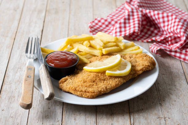 Wiener schnitzel with fried potatoes on wooden table stock photo