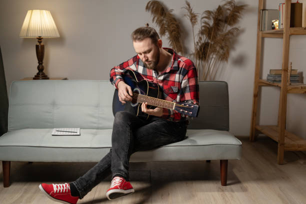 istock Young man playing guitar at home in the evening. 1472275053