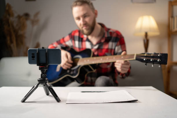 istock Teacher teaching how to play an instrument. Guitar tutorial with smartphone. Recording online music at home. 1472275129