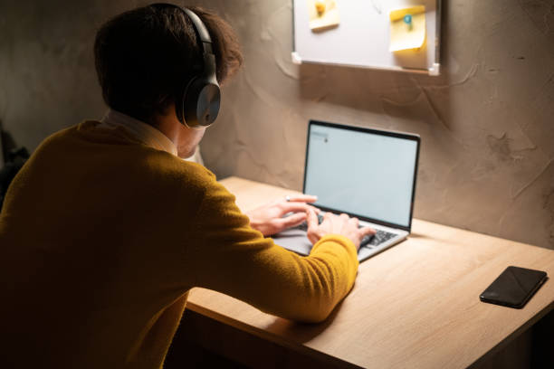 joven trabajando en una computadora portátil en la oficina en casa. estudiante masculino que estudia en el dormitorio universitario por la noche, escribiendo en una computadora portátil. - filipino ethnicity asian ethnicity men male fotografías e imágenes de stock