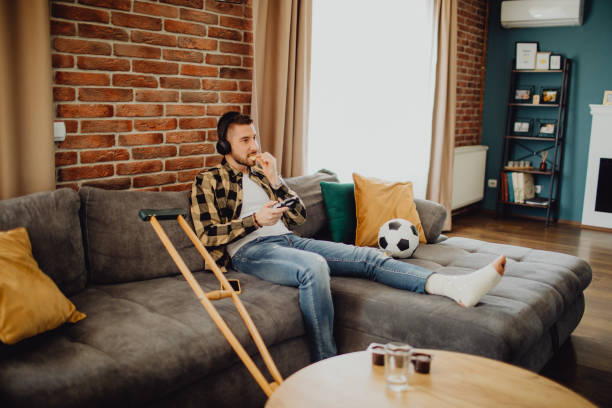 istock Young man with an injured leg playing a video game while resting at home 1472280862