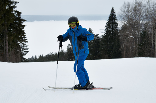 A man in blue sportswear on skis stands against the backdrop of a snowy slope