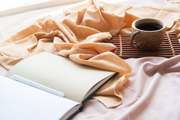 istock Coffee cup, bamboo tray and open notebook on bed. Good springtime morning. 1472285013