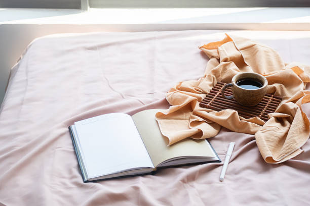 istock Coffee cup, bamboo tray and open notebook on bed. Good springtime morning. 1472285131