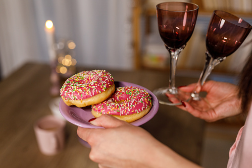 Close up shot of unrecognizable young woman serving doughnuts and wineglasses on a table when setting up for a celebratory event.