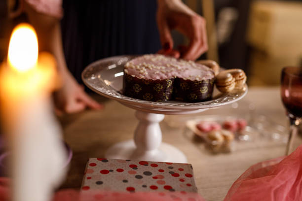 Close up shot of unrecognizable young woman arranging heart shaped macaroons around a cute small cake when setting up for Valentine's day celebration.