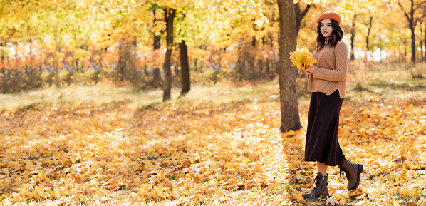 Young happy woman walking at the park. Autumn walk. Dreaming girl holding leaves bouquet. Copy space. Banner