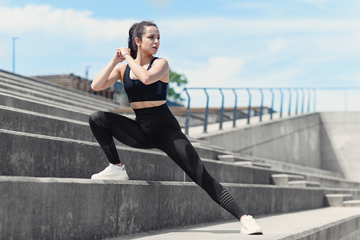 Fitness woman stretching legs on stairs outdoor. Attractive girl with fit body in sport clothes warming up, doing leg lunge exercise before training or running.