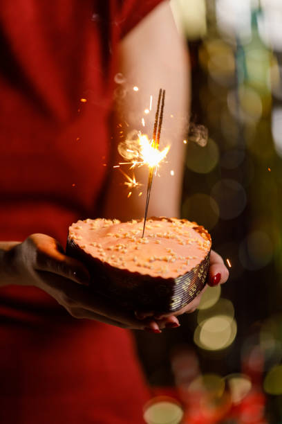 istock Young woman holding a heart shaped cake with sparklers inside burning 1472290179