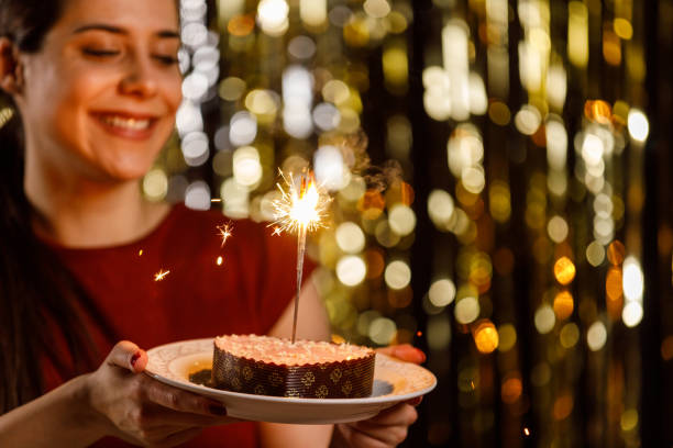istock Young woman holding a heart shaped cake with sparklers inside burning 1472290183