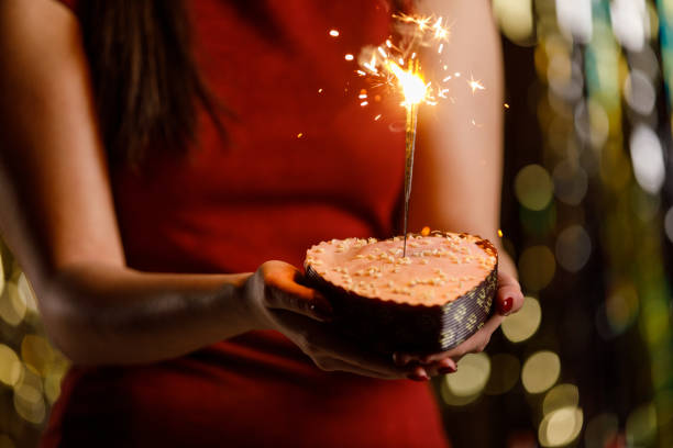 istock Young woman holding a heart shaped cake with sparklers inside burning 1472290184