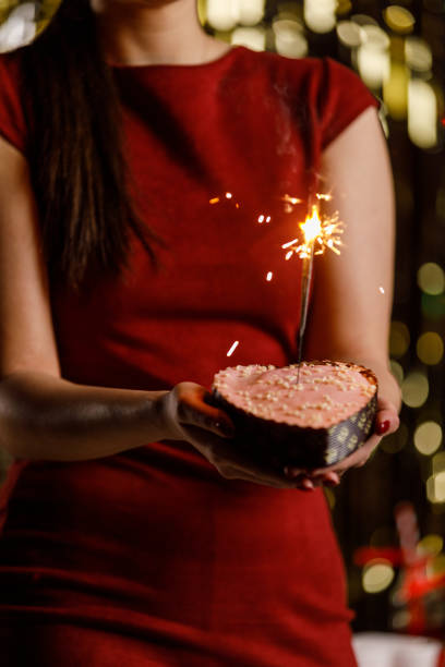 istock Young woman holding a heart shaped cake with sparklers inside burning 1472290189