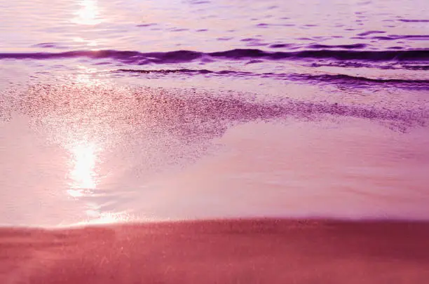 Photo of Toned purple photo of beach. Marine background. Sea coast at sunset. Glare of setting sun on wet sand