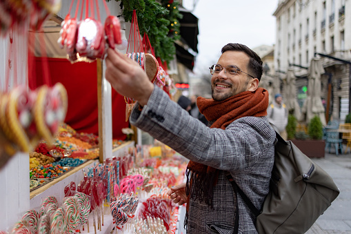 Young happy man buying candies at market stall in the city.